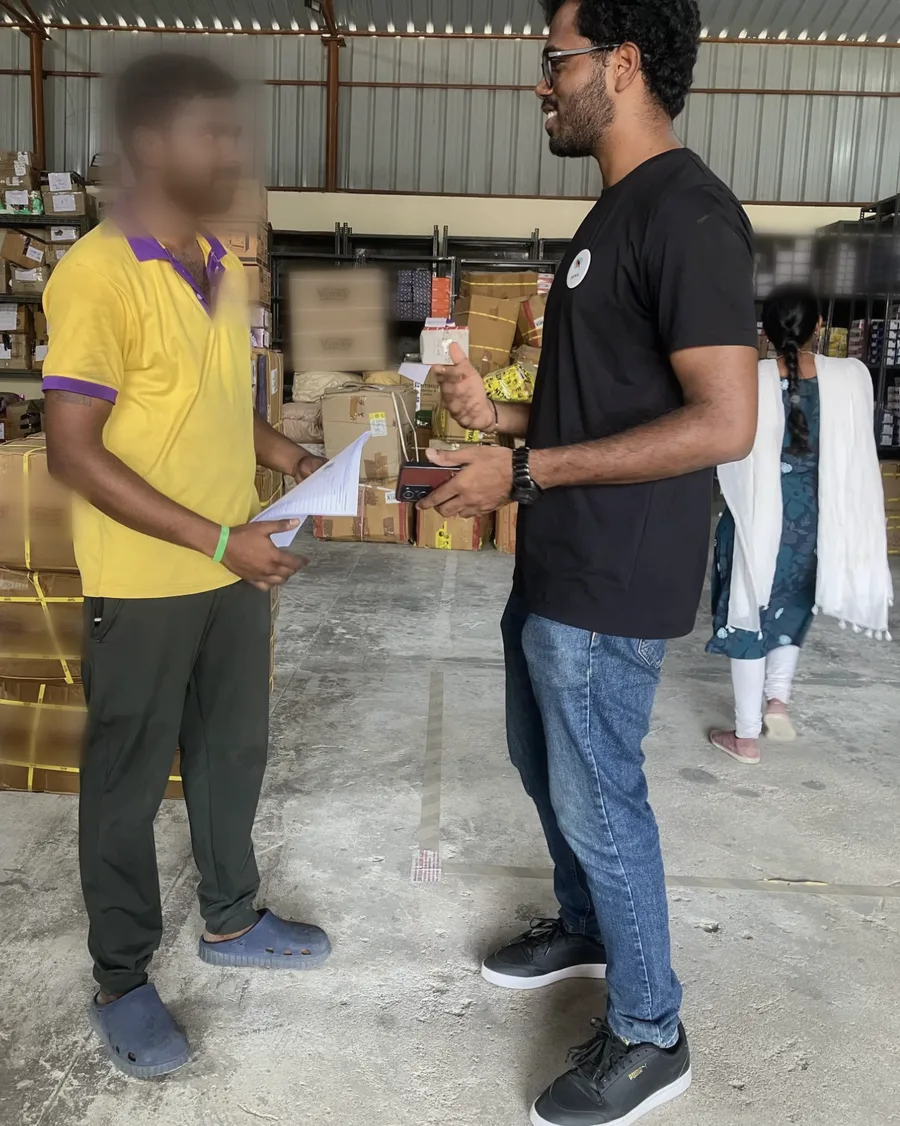A warehouse worker holding a printed order sheet talks with the author; the worker's face and company logo are blurred.