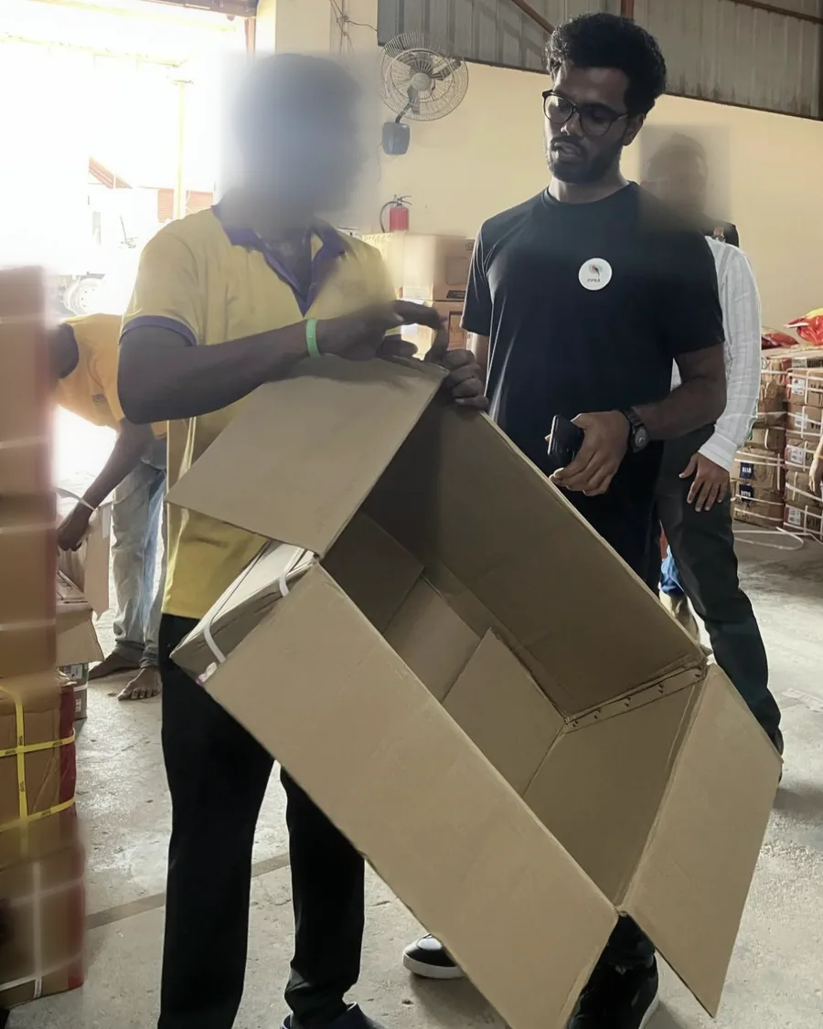 A worker opens a large empty carton to show the author how it's packed; the faces of the worker and a bystander are blurred.