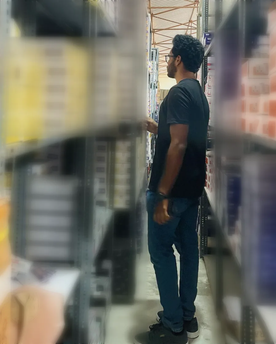 The author in a narrow aisle between tall steel racks of boxed products, looking along a shelf; product branding blurred.